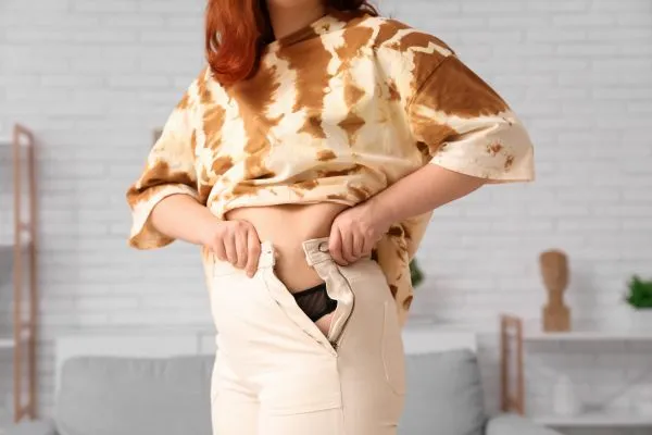 Image of woman trying to do her trousers up after pregnancy weight gain Hampton in Arden